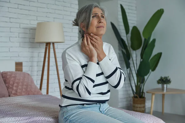 Worried Senior Woman Examining Her Neck While Sitting Bed Home — Foto de Stock