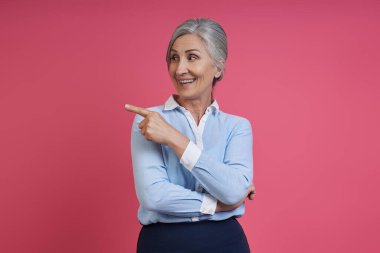 Kendine güvenen son sınıf öğrencisi kadın pembe arka planda dikilirken gülümsüyor.