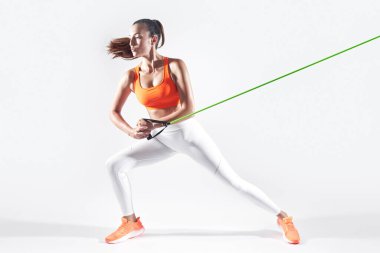 Beautiful young woman using resistance band while exercising against white background