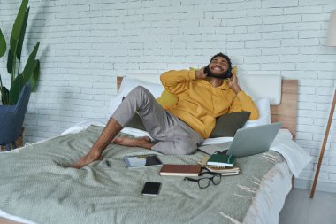 Kulaklıklı mutlu Afrikalı genç adam evde yatakta yatarken müziğin tadını çıkarıyor.