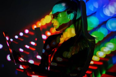 Confident woman in futuristic glasses using digital tablet against colorful background