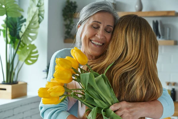 Joyful Senior Woman Embracing Her Daughter Holding Bunch Yellow Tulips — Stockfoto