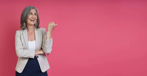 Happy Senior Woman Formalwear Pointing Away While Standing Pink Background — Stock Photo, Image