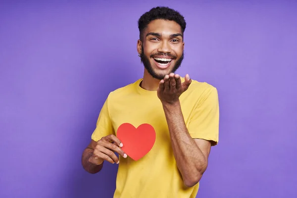 Handsome African Man Holding Paper Heart Blowing Kiss Purple Background — Stok fotoğraf