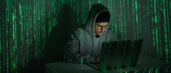 Confident young man in hooded shirt using computer against dark background