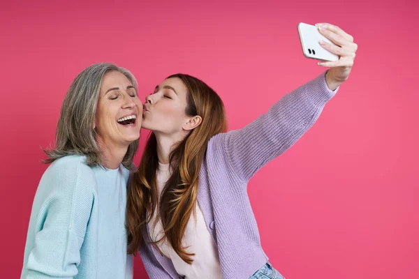 Hija Adulta Besando Madre Mientras Hace Selfie Contra Fondo Rosa — Foto de Stock