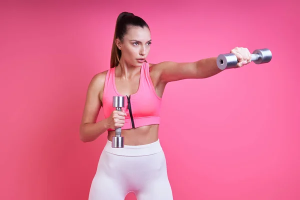 Concentrated Young Woman Sports Clothing Exercising Dumbbells Pink Background — Stockfoto