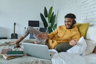 Mutlu Afrikalı adam evde yatakta yatarken internet konferansında el kol hareketi yapıyor.