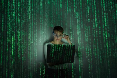 Confident woman adjusting futuristic glasses while using laptop against dark background