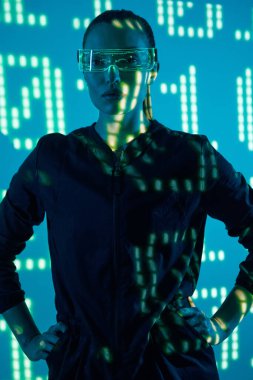 Beautiful young woman in futuristic glasses standing against colorful background