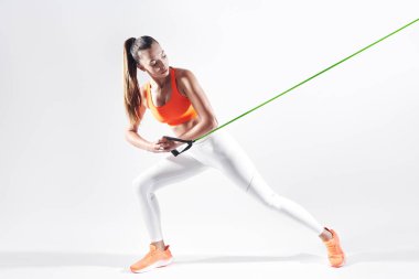 Confident young woman using resistance band while exercising against white background