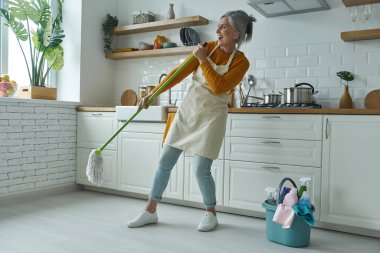 Mutfakta dururken mikrofon gibi paspas taşıyan son sınıf mutlu kadın.