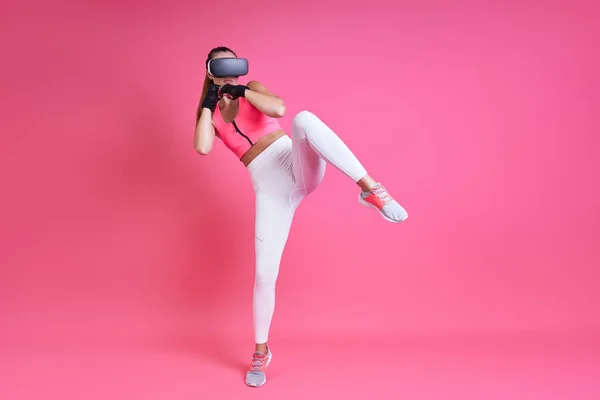 Confident Young Woman Virtual Reality Glasses Kicking Pink Background — стоковое фото