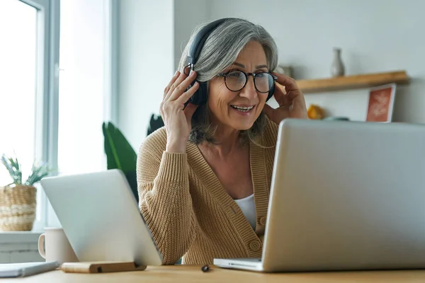 Cheerful Senior Woman Adjusting Her Headphones While Using Laptop Home — Stock Photo, Image