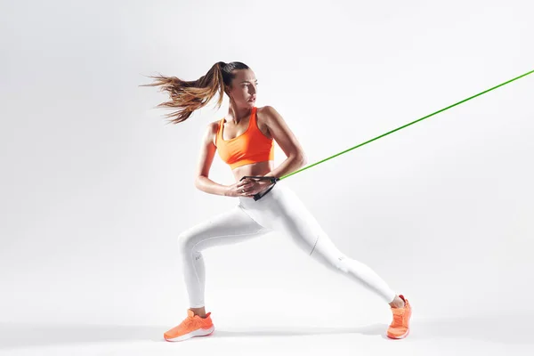 Confident Young Woman Using Resistance Band While Exercising White Background — Φωτογραφία Αρχείου