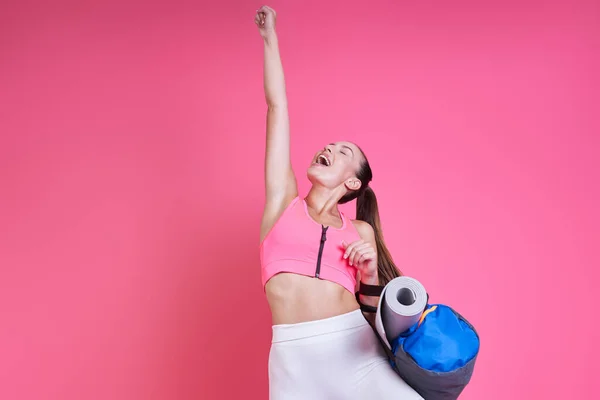 Opgewonden Vrouw Sportkleding Draagtas Houden Arm Opgeheven Tegen Roze Achtergrond — Stockfoto