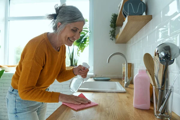 Confident senior woman tidying up the kitchen counter and smiling