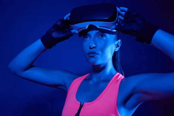 Beautiful young woman in sports clothing wearing virtual reality glasses against colorful background