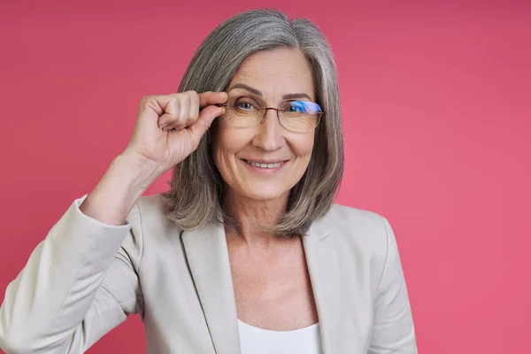 Cheerful Senior Woman Formalwear Adjusting Eyeglasses While Standing Pink Background — Foto Stock