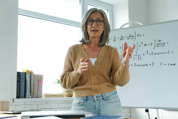 Senior woman teaching mathematics while standing near the whiteboard and gesturing