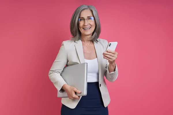 Старша Жінка Офіційному Одязі Ноутбуком Смартфоном Стоячи Рожевому Фоні — стокове фото