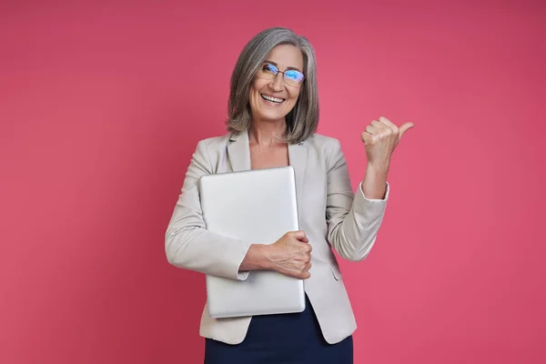 Happy Senior Woman Formalwear Carrying Laptop Pointing Away Pink Background — Foto de Stock