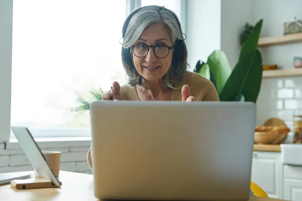 Cheerful Senior Woman Using Laptop Gesturing While Sitting Desk Kitchen — Stock Photo, Image