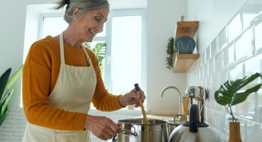 Confident senior woman smiling while cooking at the domestic kitchen