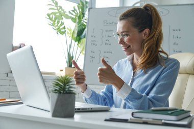 Happy woman gesturing while having web conference near the whiteboard at classroom
