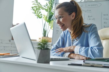 Beautiful woman using laptop while sitting near the whiteboard at classroom