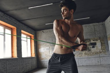 Concentrated young man exercising with elastic resistance band in gym