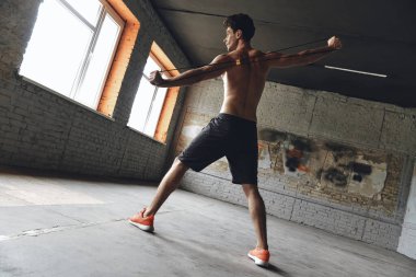 Full length of concentrated young man exercising with resistance band in gym