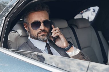 Confident mature businessman talking on mobile phone while sitting in the car