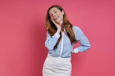 Attractive young woman touching face and smiling while standing against colored background