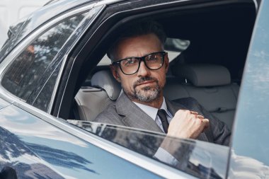 Elegant mature businessman looking through a window while sitting on the back seat of a car
