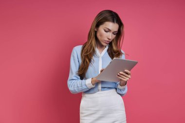 Confident young woman using digital tablet while standing against colored background