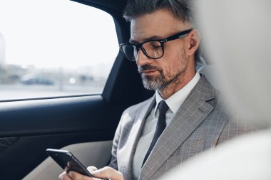 Confident mature businessman using smart phone while sitting in the car
