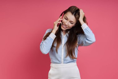 Beautiful young woman talking on mobile phone while standing against colored background