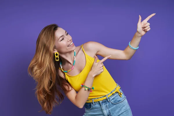 Attractive Young Woman Pointing Away Smiling While Standing Purple Background — ストック写真