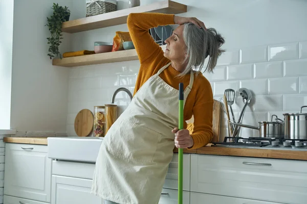 Tired Senior Woman Leaning Mop While Standing Domestic Kitchen — Stok fotoğraf