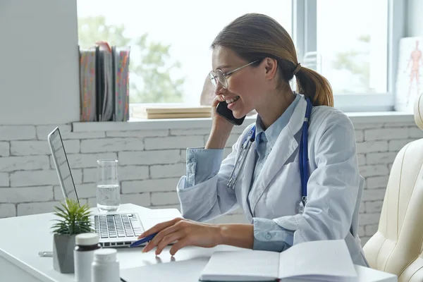 Cheerful Female Doctor Talking Phone Using Computer While Sitting Medical — Fotografia de Stock