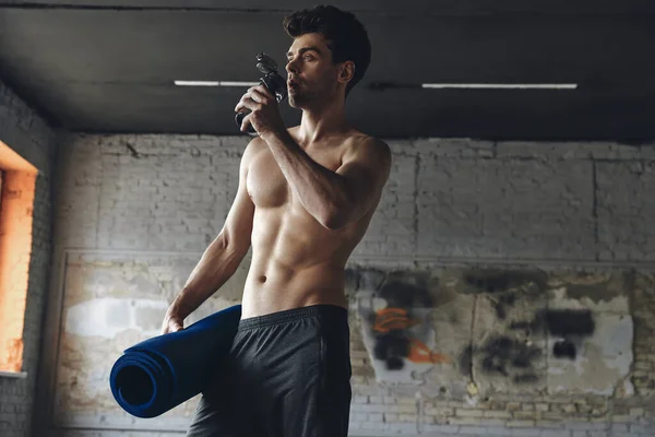 Confident Young Man Carrying Exercise Mat Drinking Water While Standing — Stockfoto