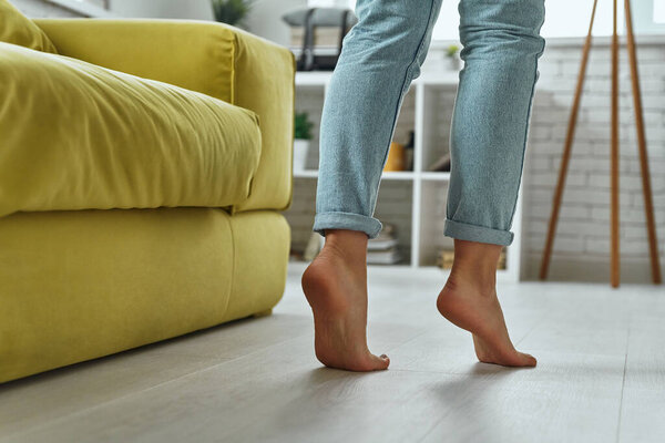 Close-up of barefoot woman walking on warm wooden floor at home