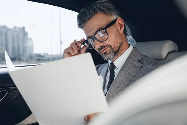 Concentrated Mature Businessman Looking Papers While Sitting Back Seat Car — Stockfoto