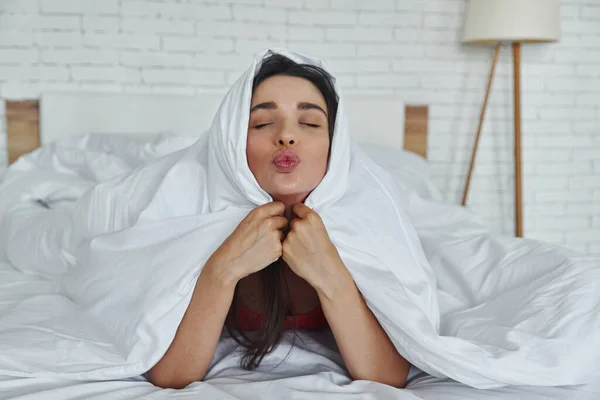 Playful Young Woman Covering Blanket Puckering While Lying Bed Home — стоковое фото