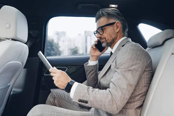 Confident Mature Businessman Using Digital Tablet Talking Phone While Sitting — стоковое фото