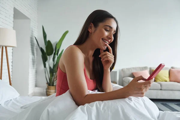 Attractive Young Woman Using Smart Phone Smiling While Sitting Bed — Stockfoto