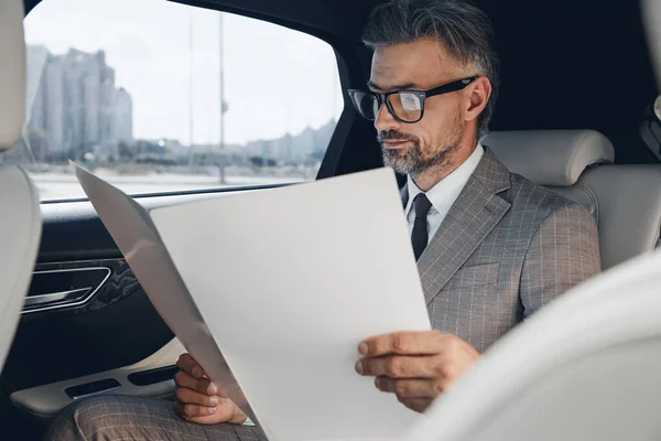 Confident Mature Businessman Looking Papers While Sitting Back Seat Car — стоковое фото