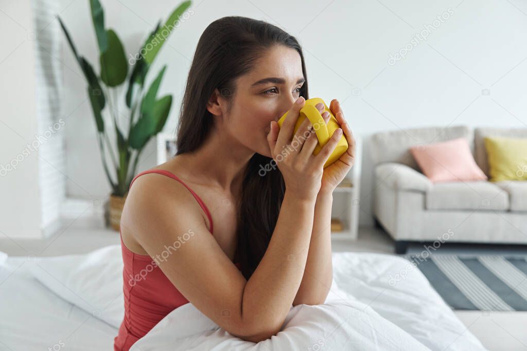 eautiful young woman enjoying hot drink after waking up in bed