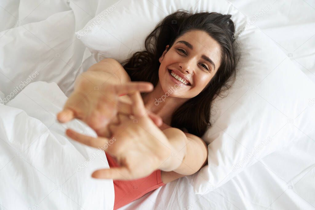 Top view of relaxed young woman keeping arms outstretched while lying in bed